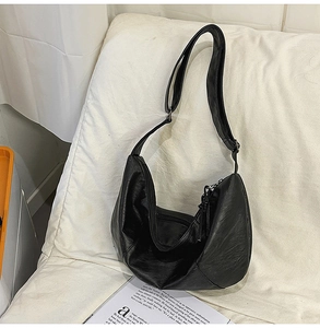 Détail du grand sac demi-lune noir avec une texture en cuir souple posé sur un coussin blanc