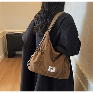 Dettaglio della borsa a tracolla in tela marrone scuro con patch Myron Bear sul cappotto