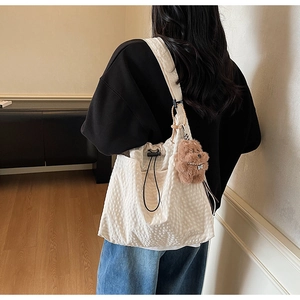Chic cream bucket bag with waffle texture and bear charm shown on shoulder model