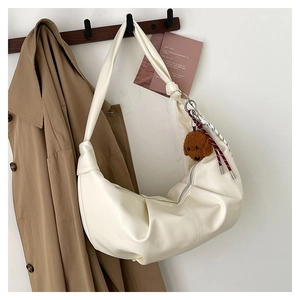 Close-up of creamy white croissant bag with plush puppy pendant on a wooden hanger