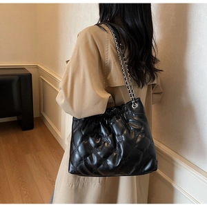 Détail du sac seau noir matelassé avec chaîne porté sur un trench-coat beige élégant