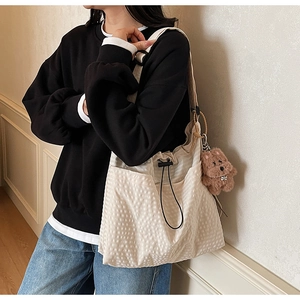 Detail of cream bucket bag showing waffle texture, black drawstring, and plush pendant