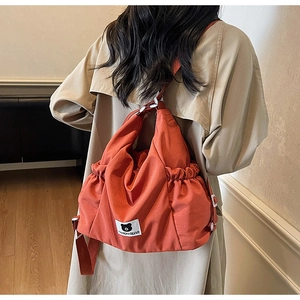 Dettaglio borsa arancione con design arricciato e patch orsetto su trench beige