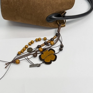 Detail of suede handbag featuring decorative wood beads and vintage silver metal tags