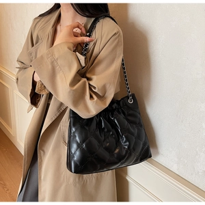 Gros plan d'un sac seau matelassé noir porté par un mannequin en trench beige