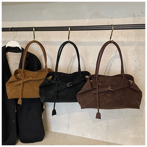 Three suede shoulder tote bags in brown, black and coffee hanging on a metal rack