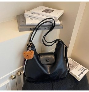 Close-up of black matte leather tote bag with embossed text and bear plush charm