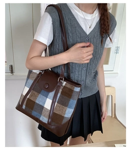 Detail of vintage plaid tote bag featuring brown leather trim and button flap closure