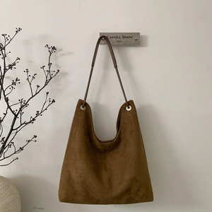 Detail of a large brown suede Hobo shoulder bag with leather straps on a white wall