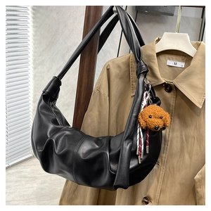 Close-up of black pleated dumpling bag with a brown plush dog charm and knotted strap