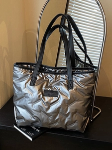 Metallic silver quilted puffer tote bag with black handles on a minimalist background