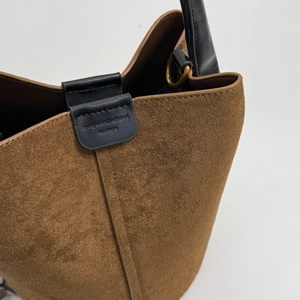 Detail of brown suede texture with brand embossing and bronze D-ring on bucket bag