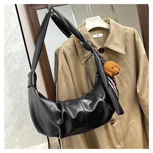 Detail of black pleated hobo bag featuring a knot handle and brown teddy bear charm