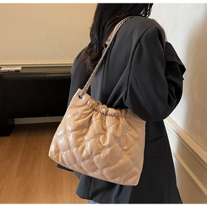 Détail du sac seau matelassé beige avec bandoulière chaîne porté à l'épaule