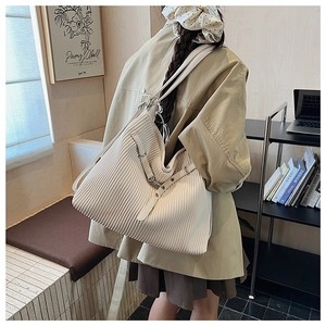 Detail of a pleated beige tote bag showing vertical folds and silver metal buckles