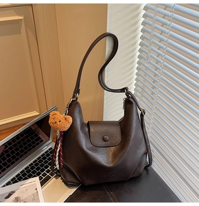 Detail of vintage brown shoulder bag featuring a cute plush bear charm and magnetic flap