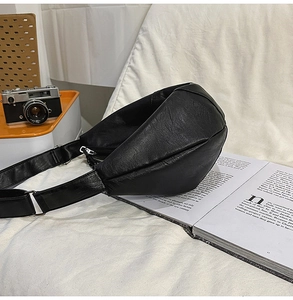 Détail du sac croissant en similicuir noir texturé posé sur un tissu blanc avec bandoulière