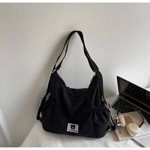 Dettaglio della borsa a tracolla in nylon nero con patch Myron Bear e tasca laterale