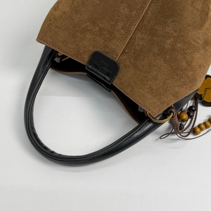 Close-up of brown suede bucket bag featuring black leather trim and ethnic bead charm