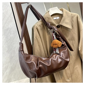 Detail of dark brown leather crescent bag with pleated design and teddy bear charm