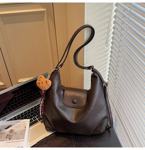 Detail of dark brown leather tote with a flap buckle, fashion imprint, and bear pendant