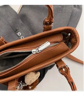 Detailed close-up of smooth metal zipper and brown lychee grain leather on handbag