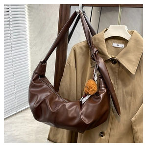 Detail of dark brown leather crescent bag with pleated texture and teddy bear charm
