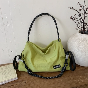 Close-up of green nylon shoulder bag with black and white woven rope handle and fashion label