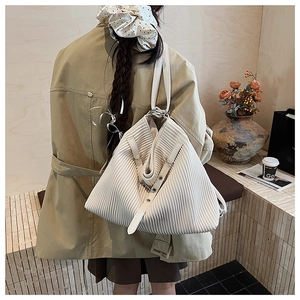 Detailed view of white pleated tote bag with leather strap worn with khaki trench coat