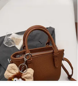 Detail of a brown lychee pattern leather tote with a decorative beige plush bow charm