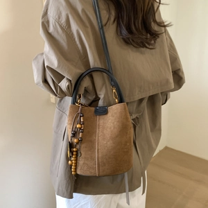 Detail of a brown suede bucket bag featuring vintage wooden bead tassels and gold hardware