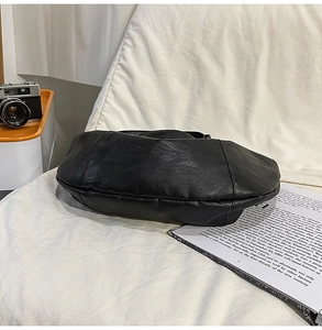 Détail du sac bandoulière noir en similicuir avec texture grainée sur tissu blanc