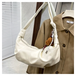 Detail of cream pleated shoulder bag with cute brown bear charm on khaki jacket