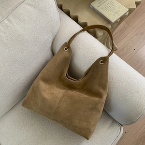Detail of vintage brown suede tote bag with metal eyelets on a cream textured sofa