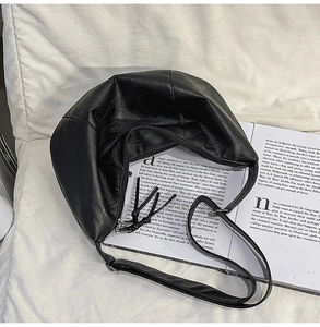 Gros plan d'un sac bandoulière noir en forme de demi-lune avec texture cuir et pompon