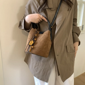 Detail view of brown matte bucket bag with black handle and wooden bead tassel decor