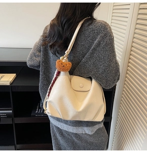 Detail of cream hobo bag with teddy charm and silk scarf worn on a knit sweater