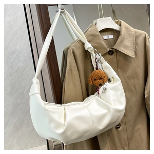 Detail of off-white pleated crescent bag with cute brown bear charm on khaki coat background