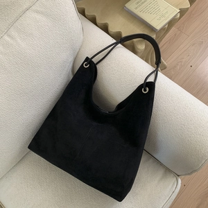 Detailed texture of black suede tote bag with silver eyelets on a cream textured sofa