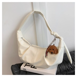 Close-up of a white crescent shoulder bag featuring pleated texture and a teddy bear charm