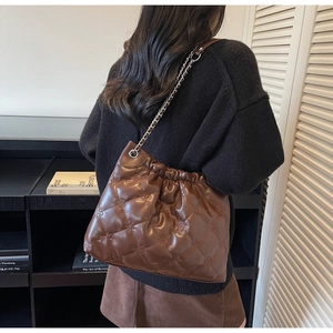 Détail d'un sac seau en cuir matelassé marron avec chaîne argentée porté par un mannequin