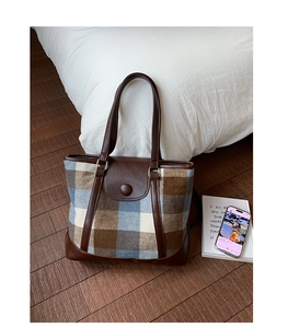 Detailed close-up of retro plaid tote bag with brown leather straps on wood floor