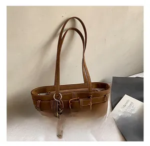 Detail of brown leather tote bag with decorative buckle strap and plush charm