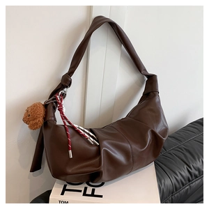Detail of dark brown leather crescent bag with plush bear charm on a stack of books