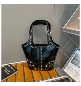Dettaglio borsa tote in ecopelle nera con borchie argentate su uno sgabello in legno