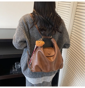 Brown leather tote bag featuring a teddy bear charm and plaid scarf on a model's shoulder