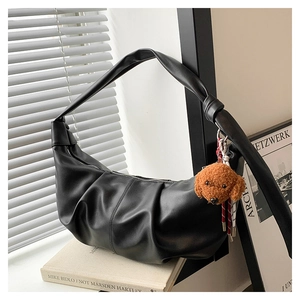 Detail of black pleated cloud bag with brown puppy charm on art books background