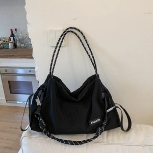 Detail of a large black tote bag featuring rope handles and fashion label accents