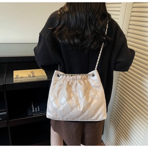 Détail du sac seau matelassé beige avec bandoulière chaîne argentée sur un mannequin