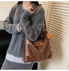 Detail of vintage brown leather tote bag with embossed text and plush bear charm